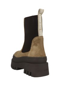 Bottine en daim marron avec des panneaux latéraux élastiques noirs, une semelle plateforme noire épaisse et une languette avec le logo "STEVE MADDEN".