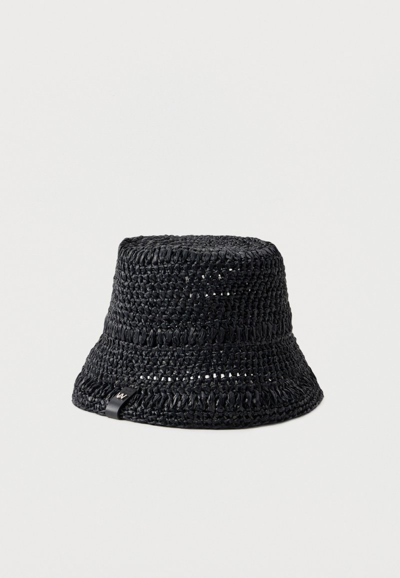 Chapeau seau tissé noir avec motif texturé et petite étiquette noire sur le bord, présenté sur un fond blanc uni.