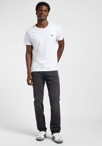 Camiseta de algodón blanca de cuello redondo con el pequeño logo negro de "Lee", combinada con jeans gris oscuro y zapatillas blancas con rayas negras.