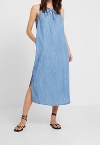 Ljusblå denim maxi-klänning med halterneck, knytning, slitsar i sidorna och avslappnad passform. Matchad med svarta sandalett med remmar.