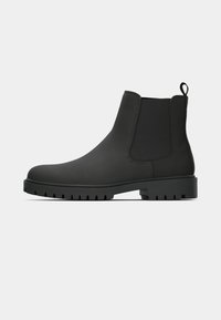 Botas Chelsea negras hechas de material suave, con paneles laterales elásticos, una lengüeta y una suela robusta con relieves para mayor tracción.