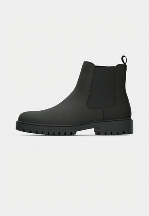 Bottes Chelsea noires en matériau lisse, avec des panneaux latéraux élastiques, une languette de tirage et une semelle robuste à crampons pour une meilleure adhérence.