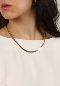 Guldtonad halsband med en slät, böjd design. Kedjan har en strukturerad yta som kompletterar en ljus överdel.