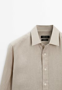 Beige Leinenhemd mit klassischem Kragen, durchgehendem Knopfverschluss und langen Ärmeln. Weiche Textur und minimalistisches Design.