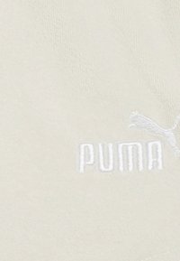 Kreemivärvi riie, millel on tekstureeritud pind, valge tikandiga "PUMA" logo ja puma siluett.