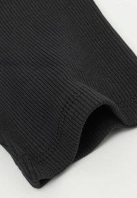 Schwarzer gerippter Stoff mit einer glatten Textur, der einen geschwungenen Saum und subtile Nähte entlang der Kante aufweist.