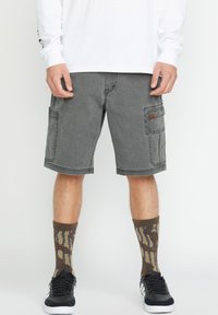 Graue Cargo-Shorts mit zwei großen Seitentaschen und kontrastierenden Nähten. Kombiniert mit gemusterten braunen und beigen Socken sowie schwarzen Sneakers.