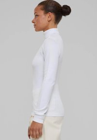 Maglione bianco a collo alto con maniche lunghe e polsini a coste, design aderente e texture liscia, visto di lato.