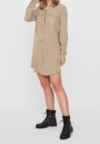 Beige skjortklänning med långa ärmar, knapprad fram, två bröstfickor, rundad nederkant, strukturerad tyg, kombinerad med svarta snörkängor.