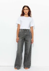 T-shirt blanc à col rond associé à un jean gris taille haute et évasé. Le jean présente une fermeture à bouton et un délavage subtil.