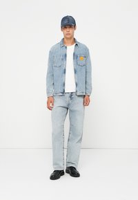 Lett blå denimjakke med to frontlommer, kombinert med lyseblå jeans. Hvit T-skjorte under og mørke sko. Caps i mørkere denim.