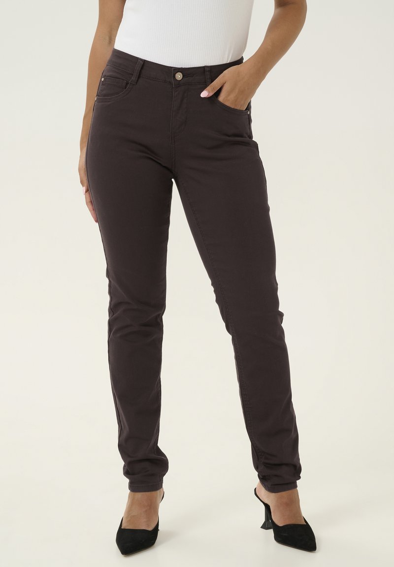Jeans skinny marroni scuri realizzati in cotone misto, con vita media, tasche frontali e chiusura a un bottone. Tessuto liscio e design aderente.