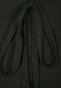 Černý top z látky s uzlem vpředu. Materiál působí měkce s texturovaným povrchem, zdůrazňujícím pohodlí a snadnost nošení.