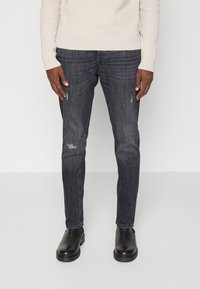 Jeans de corte slim, cinza escuro, com ligeira desgastação e leve desgaste; combinados com botas de tornozelo pretas e um suéter creme com relevo.