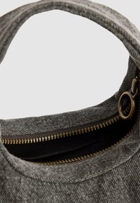 Graue Stofftasche mit einer strukturierten Oberfläche, goldenem Reißverschluss und einem runden Griff. Das Innere hat eine dunkle Fütterung und einen sichtbaren Reißverschluss.