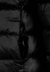 Surface d'une veste matelassée noire avec des sections piquées et une texture lisse et brillante. Le matériau semble léger et résistant à l'eau.