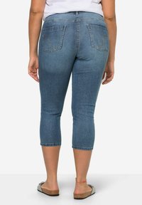 Jeans capri de mezclilla azul con un diseño ajustado, cintura de altura media y dos bolsillos traseros. Presentan detalles de costura y un corte a la altura del tobillo.