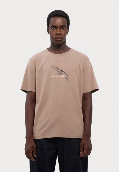 Beige Baumwoll-T-Shirt mit kurzen Ärmeln, das auf der Vorderseite einen grafischen Druck einer Hand und den Text "FILLING PIECES" zeigt. Legere Passform und einfarbig.