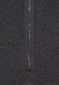 Manta de lana negra con una cinta de satén de Calvin Klein con logotipo en relieve, que muestra una textura suave y un diseño de color sólido.