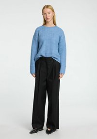 Lyseblå strikket sweater med et tekstureret mønster og dropped shoulders, parret med højhalsede sorte vidde bukser og sorte spidse sko.