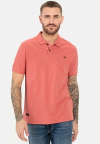 Korte mouwen koraalpoloshirt van zachte katoen, met een twee-knopen sluiting en een klein logo op de borst. Draagt bij blauwe jeans.