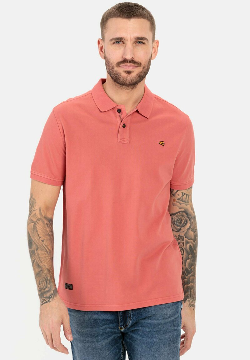Korte mouwen koraalpoloshirt van zachte katoen, met een twee-knopen sluiting en een klein logo op de borst. Draagt bij blauwe jeans.