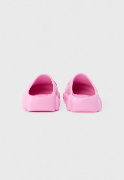 Sabots roses à enfiler en plastique lisse et durable, au design arrondi et dos ouvert, avec une semelle texturée et de légères décorations latérales.