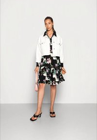 Jaqueta de denim branca curta sobre um vestido preto com padrão floral. O vestido apresenta padrões florais coloridos, e o conjunto é complementado com sandálias de salto pretas e uma bolsa rosa.