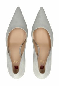 Tacones de ante gris claro, con punta afilada y una textura suave, con lados abiertos y acentos dorados en el interior. Presenta un detalle cuadrado rojo en la suela.