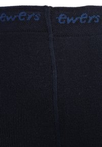 Svarte strikkede leggings med en jevn tekstur, som har et blått merkenavn langs livet. Stoffet virker elastisk og tettsittende.
