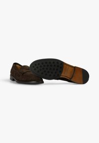 Mocasines de ante marrón con una banda decorativa, punta redondeada y suela de goma negra contrastante con patrones de agarre elevados.