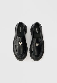 Black loafers with a smooth leather finish, rounded toe, thick textured sole, and a silver heart accent on the strap.