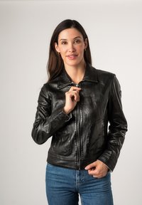 Zwarte leren jas met een kraag, ritssluiting en gestikt detail. Draag met blauwe jeans, met een soepele textuur.