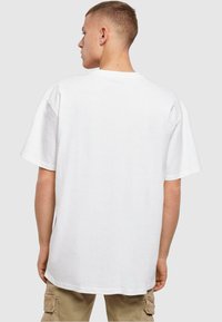 Witte korte mouwen t-shirt, relaxte pasvorm, ronde hals, gladde textuur, eenvoudige uitstraling, gedragen met beige cargobroek, weergegeven vanuit de achterkant.