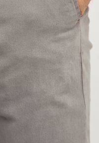 Grå denimjeans med en glat overflade, der har svage diagonale striber, standardlommer og en let indsnævret benstil.