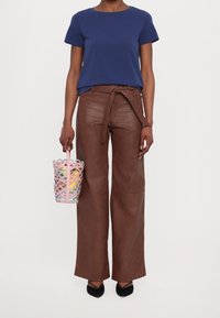Camisa azul de manga corta, pantalones de cuero marrones de talle alto con un cinturón, y un bolso tipo cubo de colores pasteles con un diseño recortado. Zapatos negros.