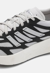 Chaussure de sport grise et noire avec tissu en maille, superpositions texturées et accents blancs. Caractéristiques des lacets fins et une semelle rembourrée.