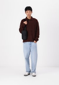 Maglione marrone a maglia testa di moro con colletto, abbinato a jeans baggy azzurri chiari. Borsetta nera a tracolla con dettagli di zip. Sneakers bianche.