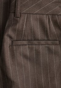 Rjava herringbone tkanina z belimi črtami, ki ima raven žepni detajl. Material se zdi gladek z rahlim leskom.