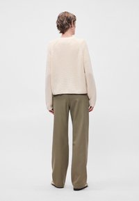 Μπεζ πλεκτό πουλόβερ με μακριά μανίκια, ριγωτή υφή, στρογγυλή λαιμόκοψη, συνδυασμένο με ελαιοπράσινα παντελόνια φαρδιάς γραμμής.