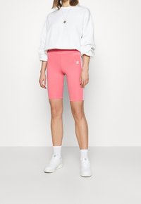 Růžové cyklistické šortky z pružné látky, s bílým logem a bočními pruhy, doplněné o bílou krátkou mikinu a bílé tenisky.