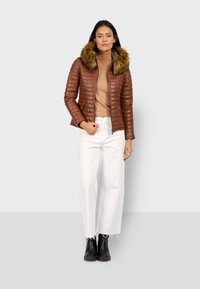 Bruine gewatteerde pufferjas met een nepbont capuchon, gecombineerd met een beige coltrui en witte wijde broek. Zwarte enkellaarsjes maken de look af.