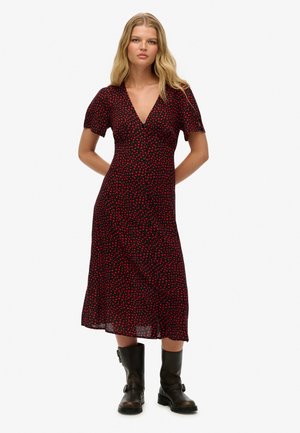 Rotes und schwarzes, mittellanges Kleid mit kurzen Ärmeln, V-Ausschnitt und einem kleinen Herzmuster, kombiniert mit schwarzen Stiefeletten.