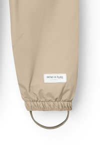Beige Regenjacke mit elastischer Manschette, ausgestattet mit einem runden Schlaufen und einem weißen Etikett mit dem Text "MINI A TURE COPENHAGEN". Glatte Textur.