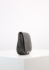 Musta nahkainen olkalaukku, jossa on teksturoitu käärmekuvio, kaartuva muoto, kiillotetut hopeanväriset metalliosat ja läppäkiinnitys.