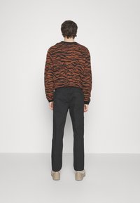 Orange and black striped sweater with a relaxed fit, paired with black trousers and tan shoes, visible from the back against a white background.