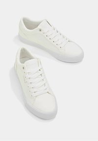 Weiße Sneaker aus Kunstleder mit glatter Textur, kontrastierenden Gummisohlen, runder Zehenpartie und Schnürverschluss. Minimalistisches Design mit dezentem Branding.