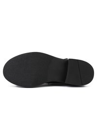 Semelle de chaussure noire avec une surface texturée, comportant un talon légèrement surélevé et une zone des orteils plate. Détails de taille en relief clairement visibles.