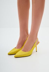 Keltaiset avokärkiset korot, joissa on ohut stiletto-korko ja avonainen takaosa. Materiaali on teksturoitua. Sopii muodollisiin tilaisuuksiin.