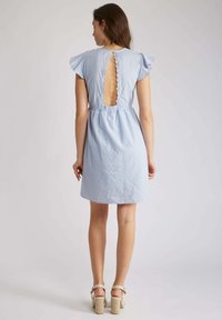 Robe rayée bleu clair avec une découpe au dos, des manches volantes et une taille smockée. Le tissu semble texturé et doux.